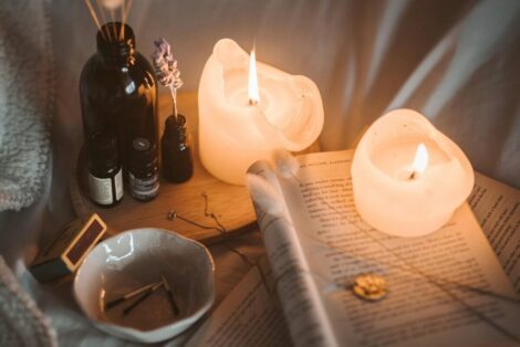 Lighted Candle on White Book Beside Black Glass Bottle